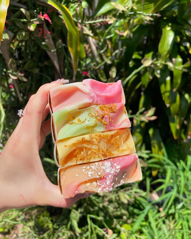 Four soap bars with calendula and oat toppings held up in a garden