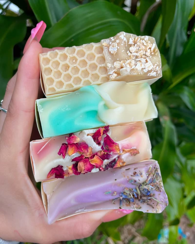 Four handmade soap bars held in a hand against green leaves